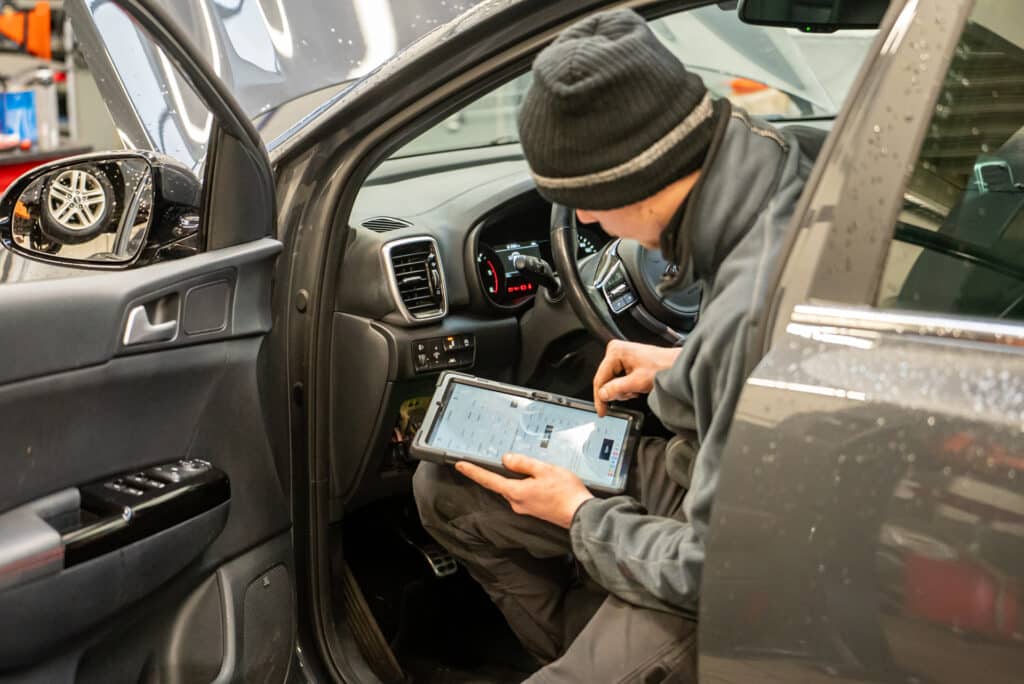 Mécanicien du garage Incar Motor à Angleur utilisant une tablette pour réaliser un rapport détaillé sur un véhicule en service d'entretien.